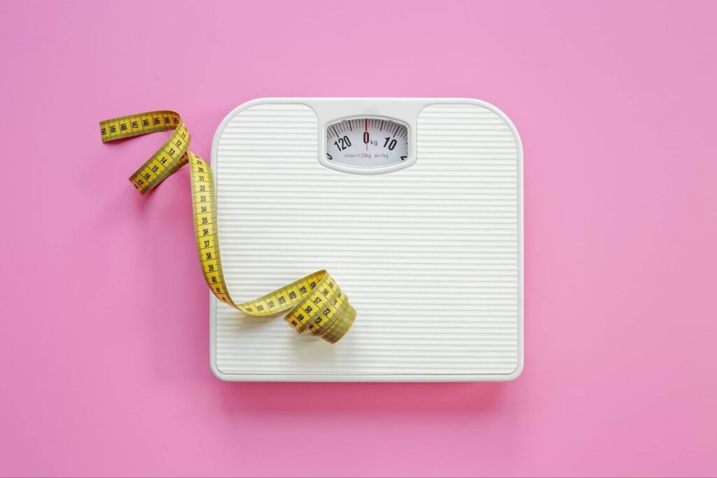 A set of bathroom scales and a measuring tape on a pink background.