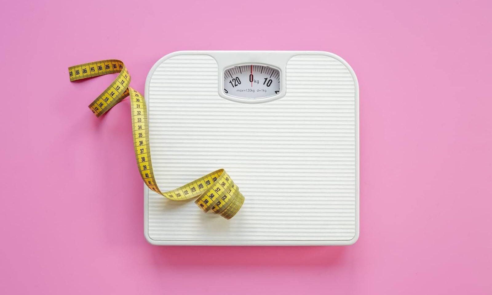 A set of bathroom scales and a measuring tape on a pink background.