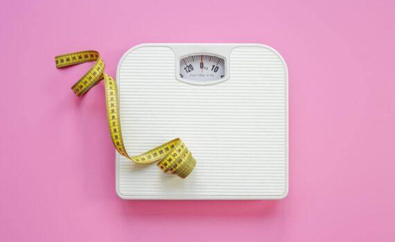 A set of bathroom scales and a measuring tape on a pink background.