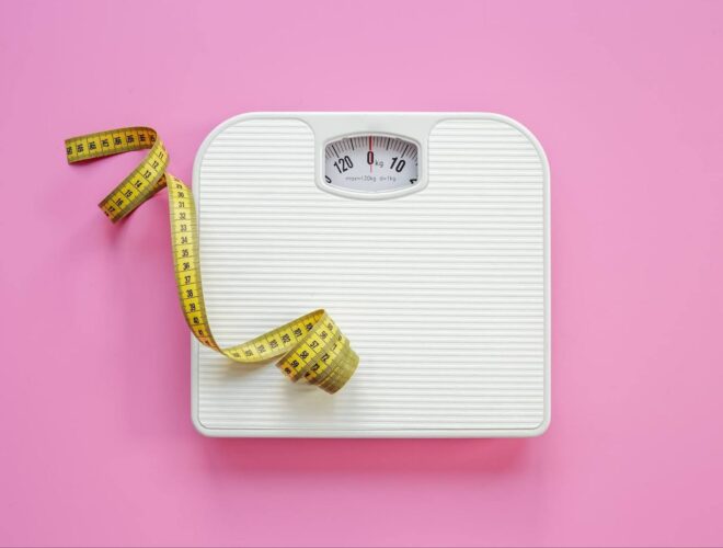 A set of bathroom scales and a measuring tape on a pink background.